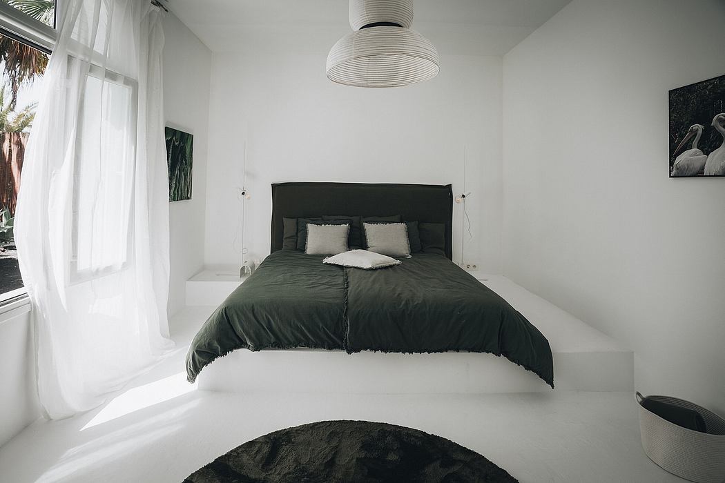 Minimalist bedroom with large window, pendant lamp, and dark green bedding.