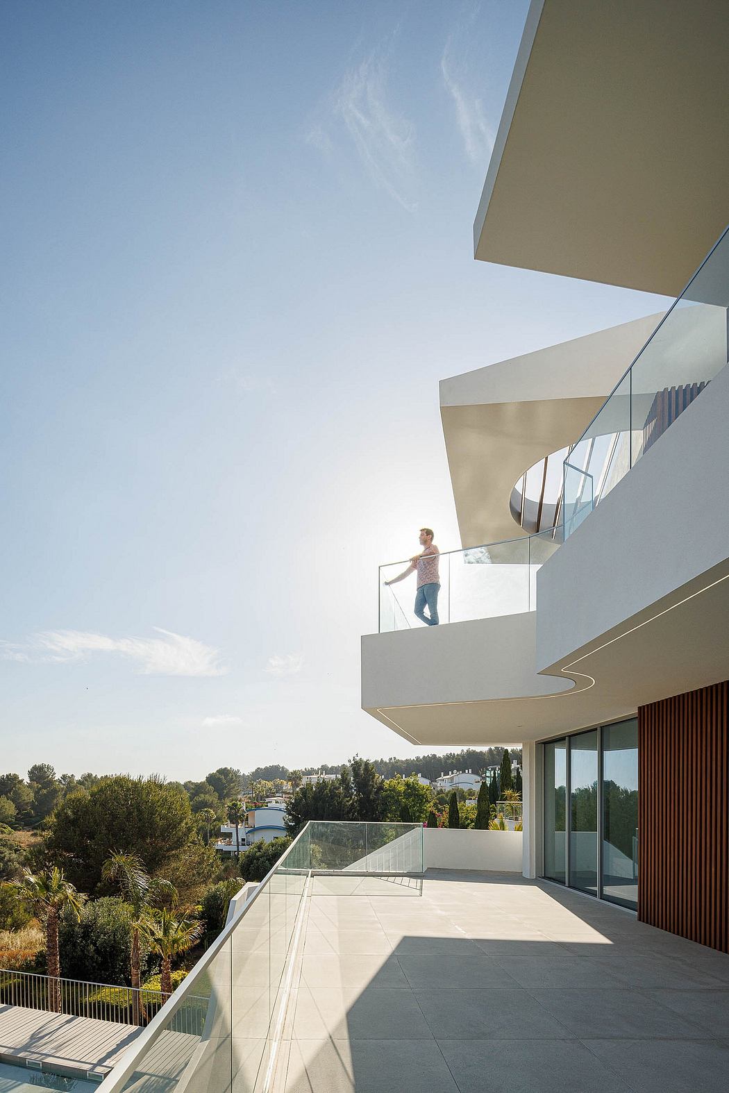 A modern, minimalist building with glass walls, cantilevered balconies, and lush landscaping.