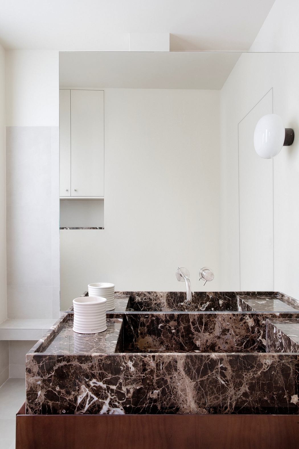 Minimalist bathroom with dark marble vanity, recessed shelving, and wall-mounted faucet.