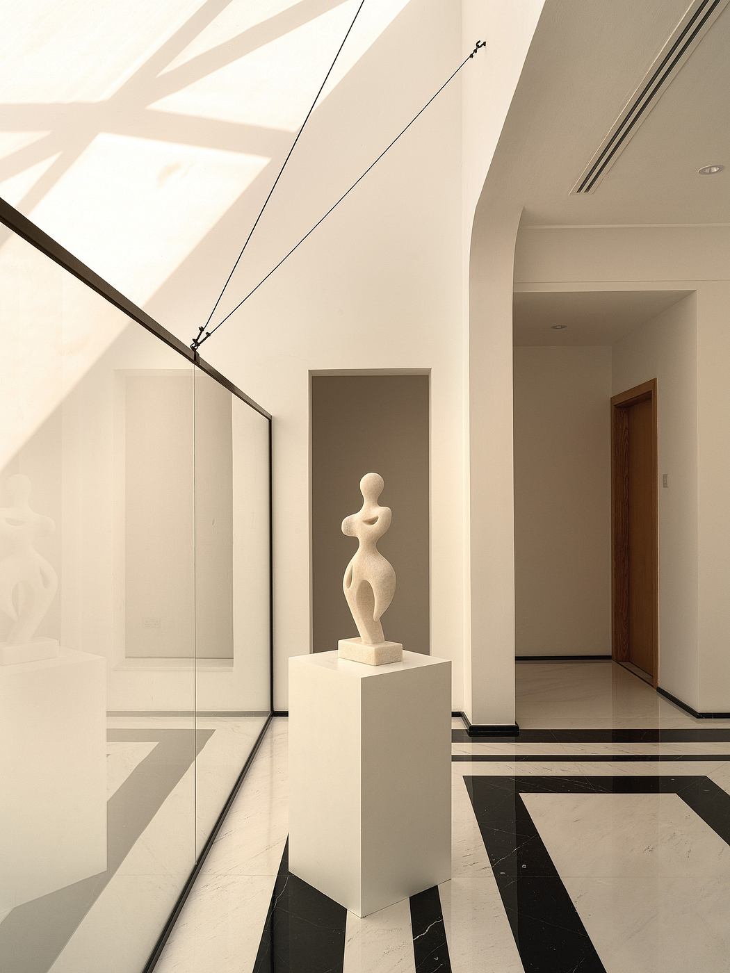 Sleek, minimalist interior with sculptural figure on pedestal and geometric lighting.