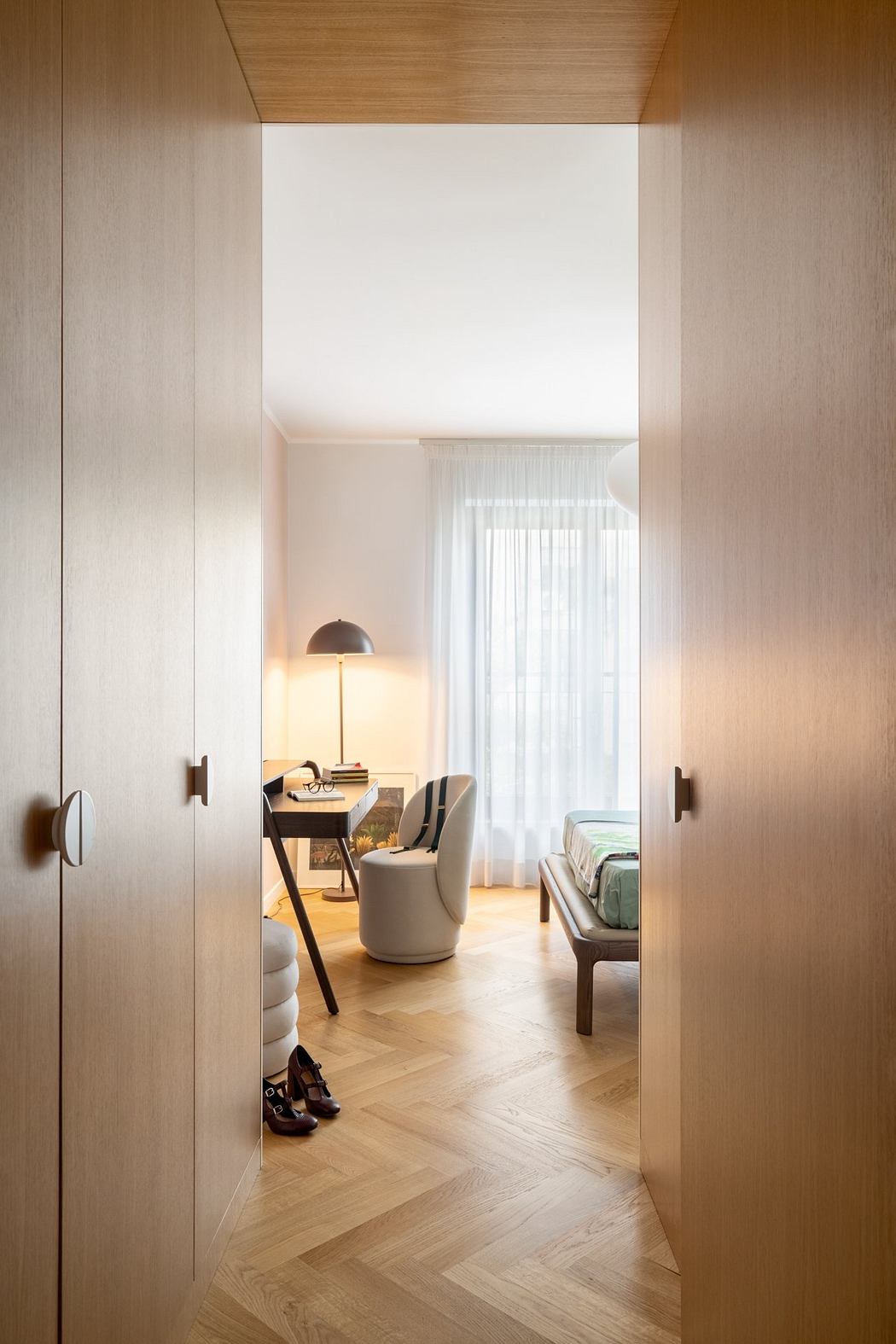 A cozy bedroom with a wooden-paneled wall, a desk, and a curtained window, creating a warm, inviting atmosphere.