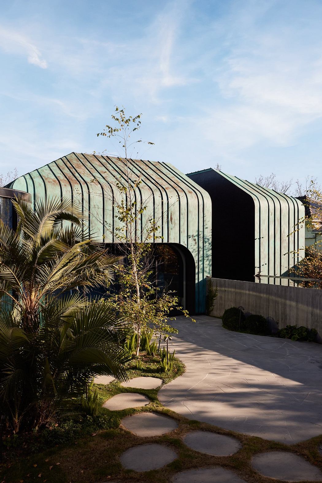 A modern, glass-enclosed structure with a sloping, metallic roof surrounded by lush tropical foliage.