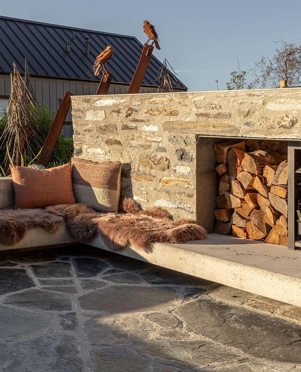 Rustic stone wall, wooden beams, and cozy outdoor seating area with fur cushions.