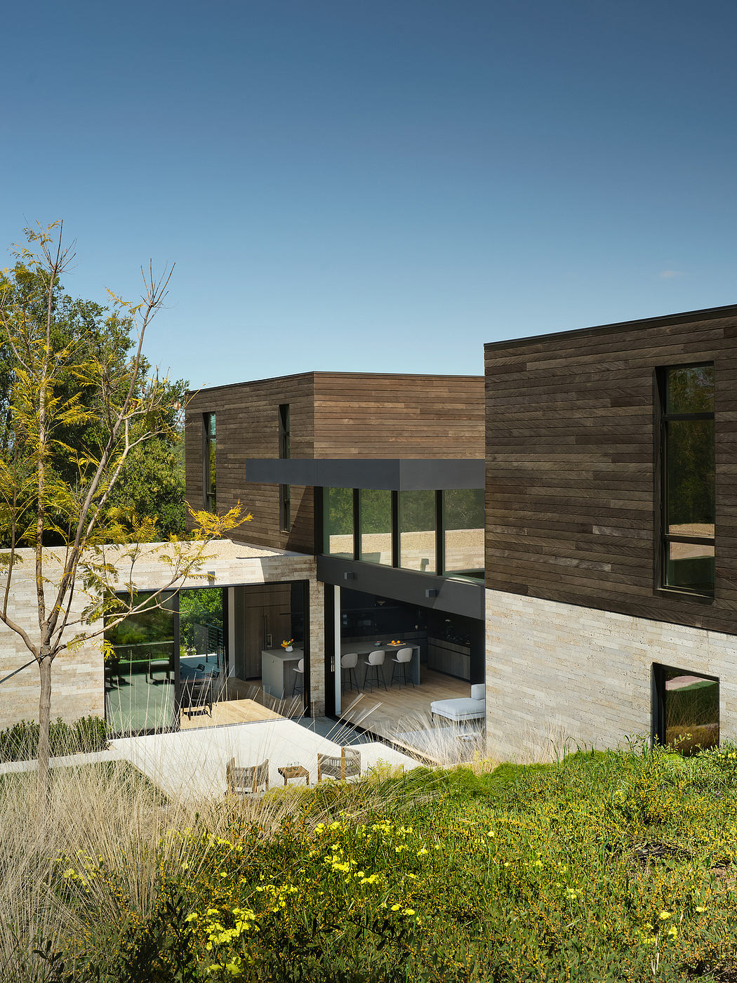 Modern, wooden exterior with large windows overlooking lush greenery and outdoor patio.