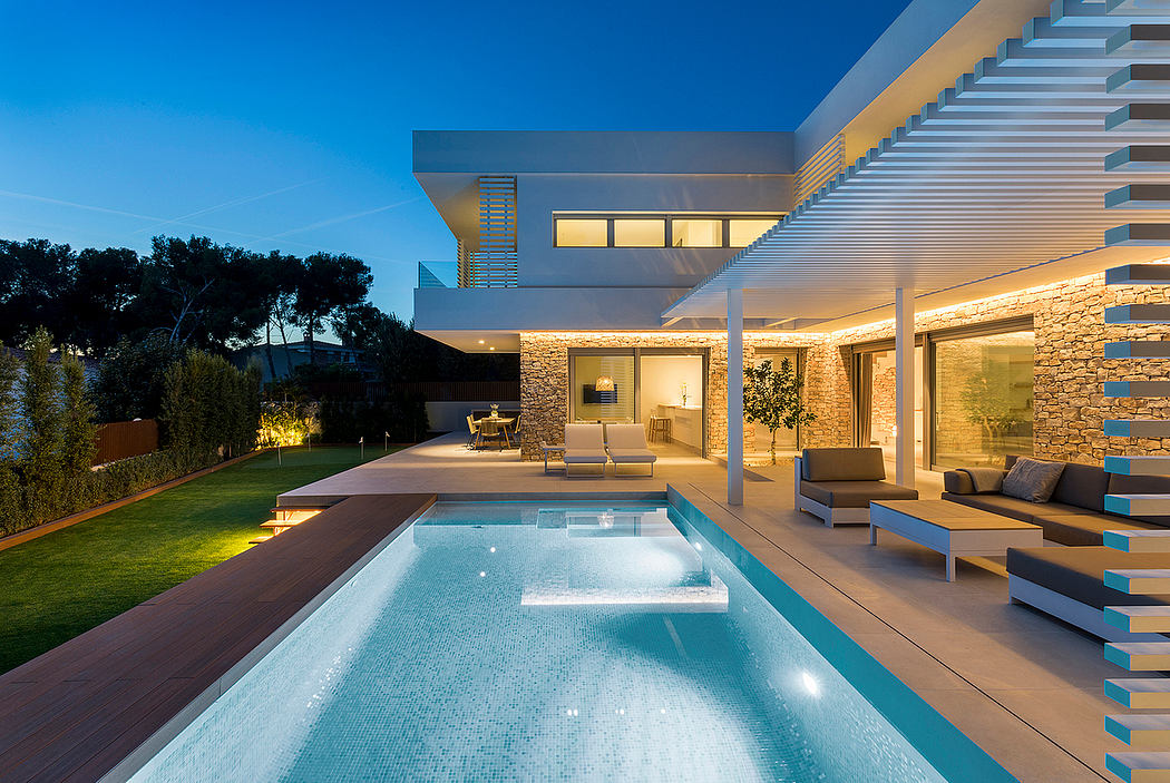 A modern, multi-level house with an illuminated pool and outdoor lounge area.