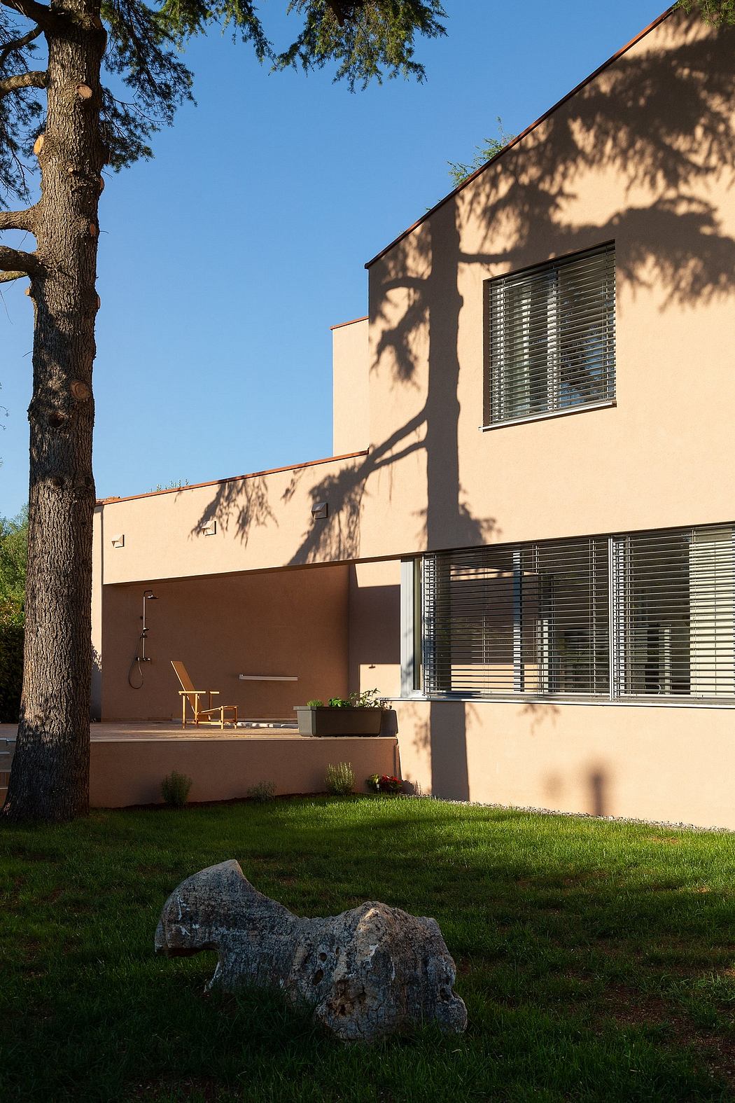 A modern, minimalist home with a wooden deck, metal railings, and large windows surrounded by trees.