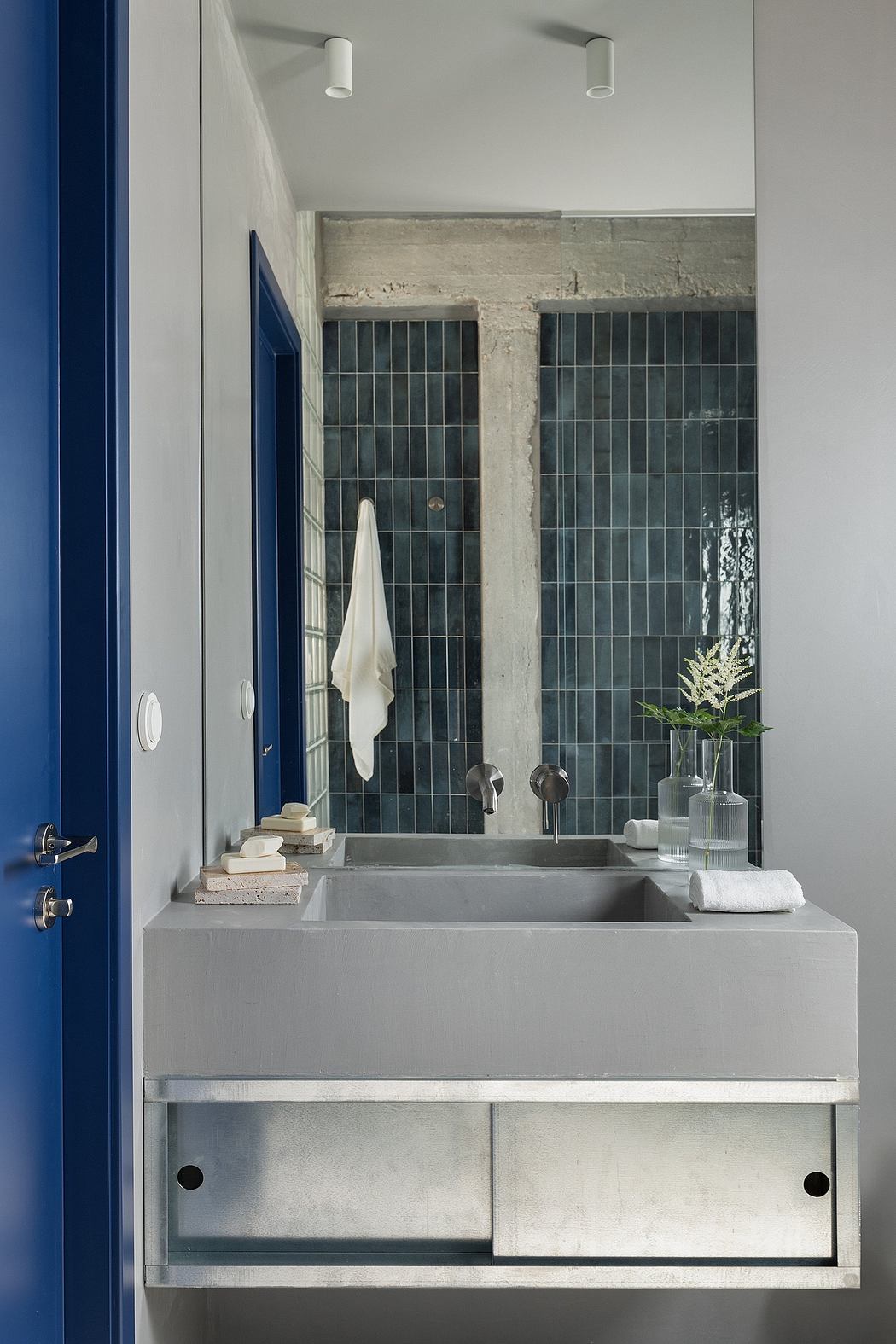 Minimalist bathroom design featuring a concrete vanity, black tile, and subtle natural accents.