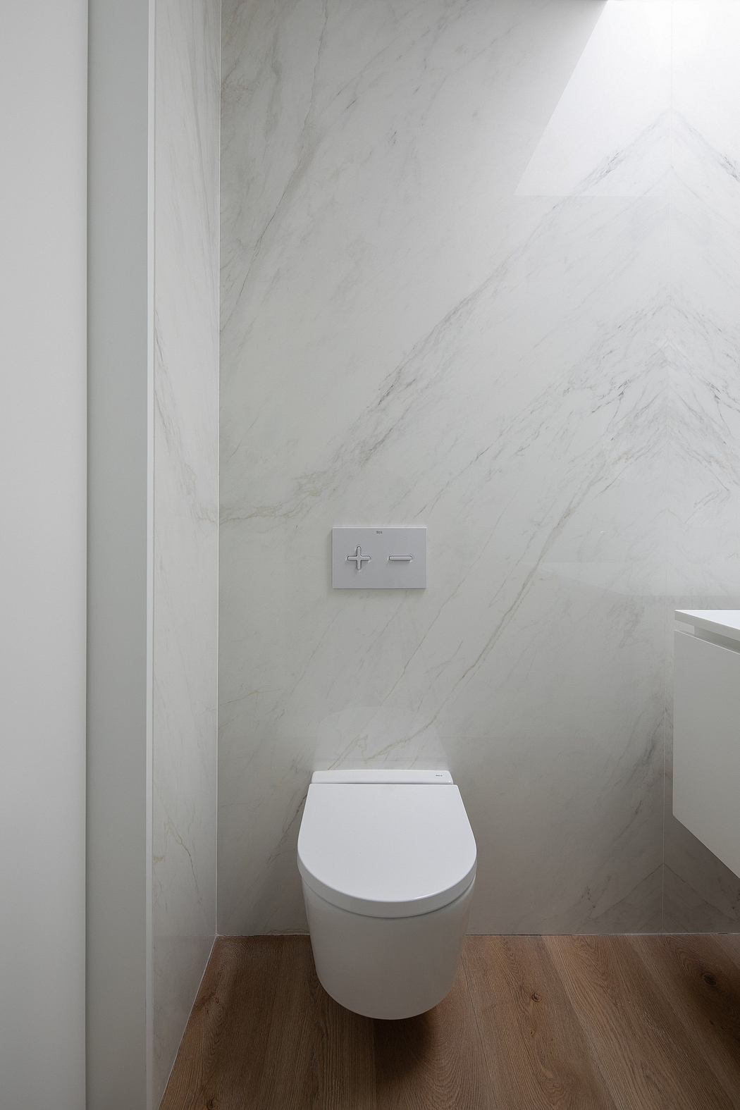 A modern bathroom with a white toilet and marble wall tiles, featuring a minimalist flush control.