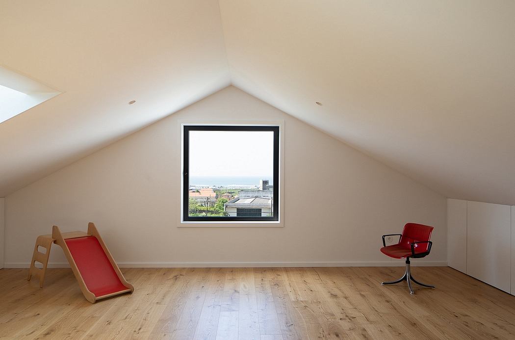 Bright attic room with slanted ceiling, wood flooring, and large window overlooking cityscape.