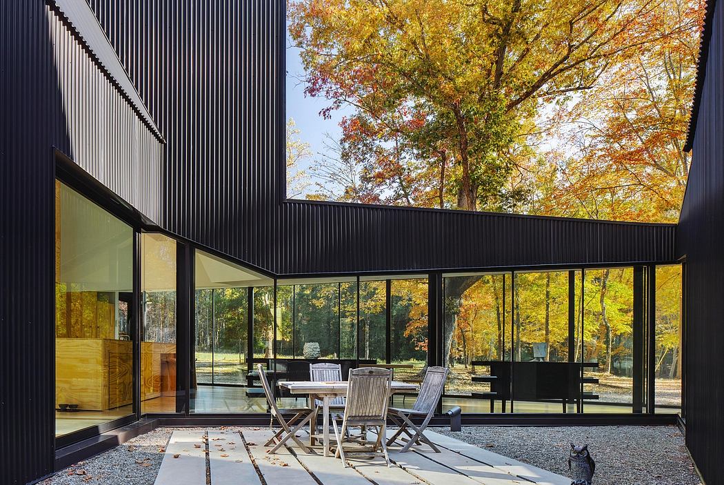 A modern, glass-enclosed structure with a sleek black exterior and mid-century furniture surrounded by a lush, autumnal landscape.
