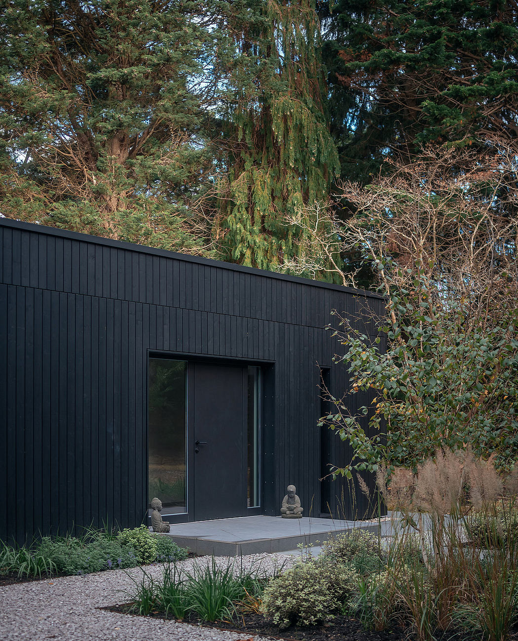 Sleek, modern black facade contrasts with lush, natural surroundings. Minimalist garden path leads to entrance.