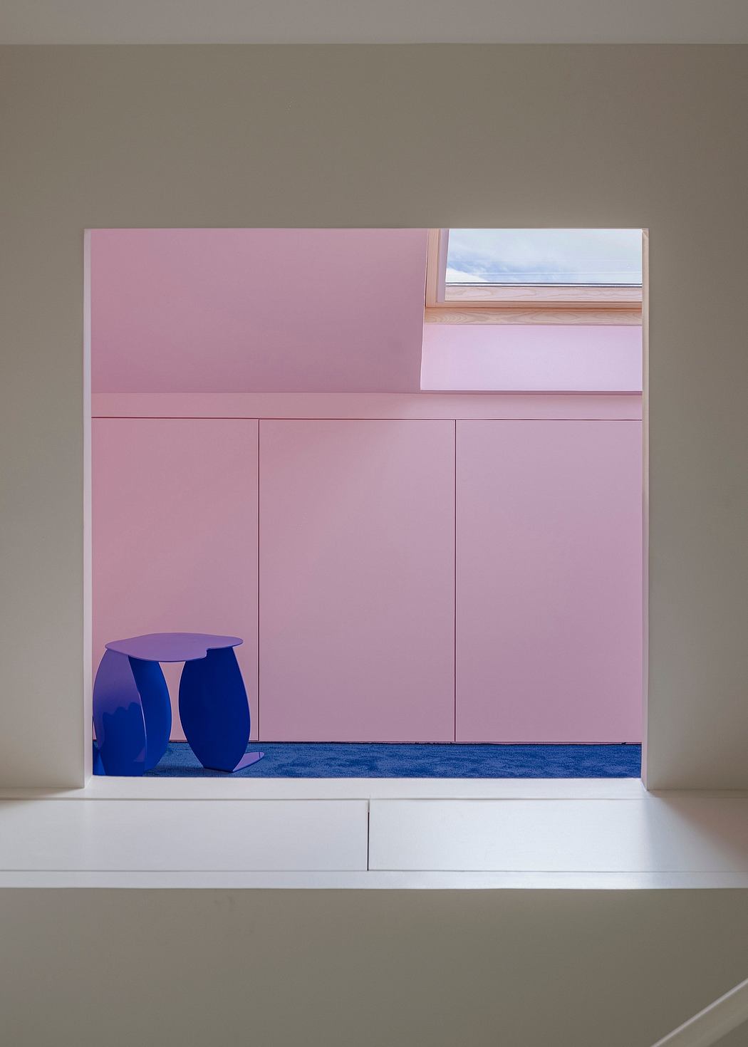 A sleek, minimalist built-in cabinet with pink panels, blue stools, and a window offering a view.
