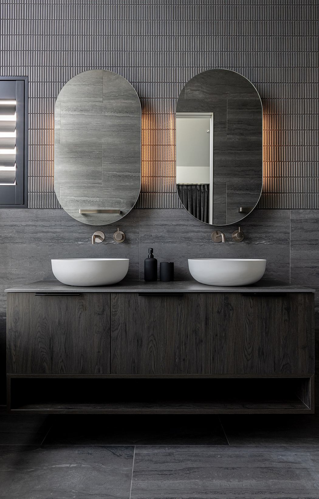 A modern, minimalist bathroom vanity with oval mirrors, vessel sinks, and a ribbed tile wall.