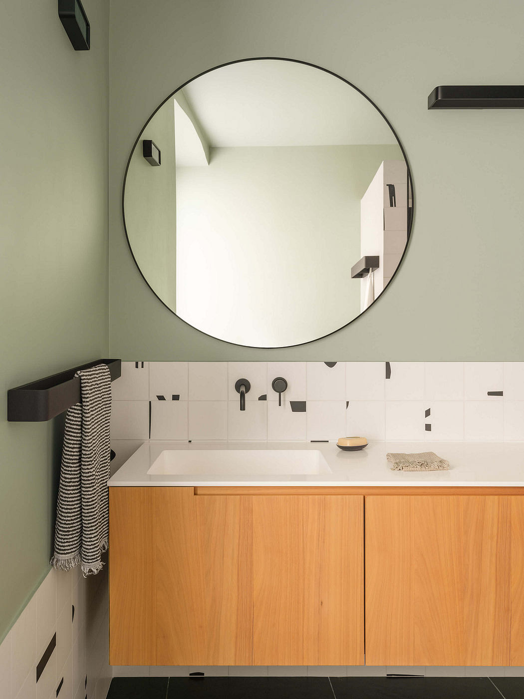 Minimalist bathroom design with round mirror, wooden vanity, and geometric tiled wall.