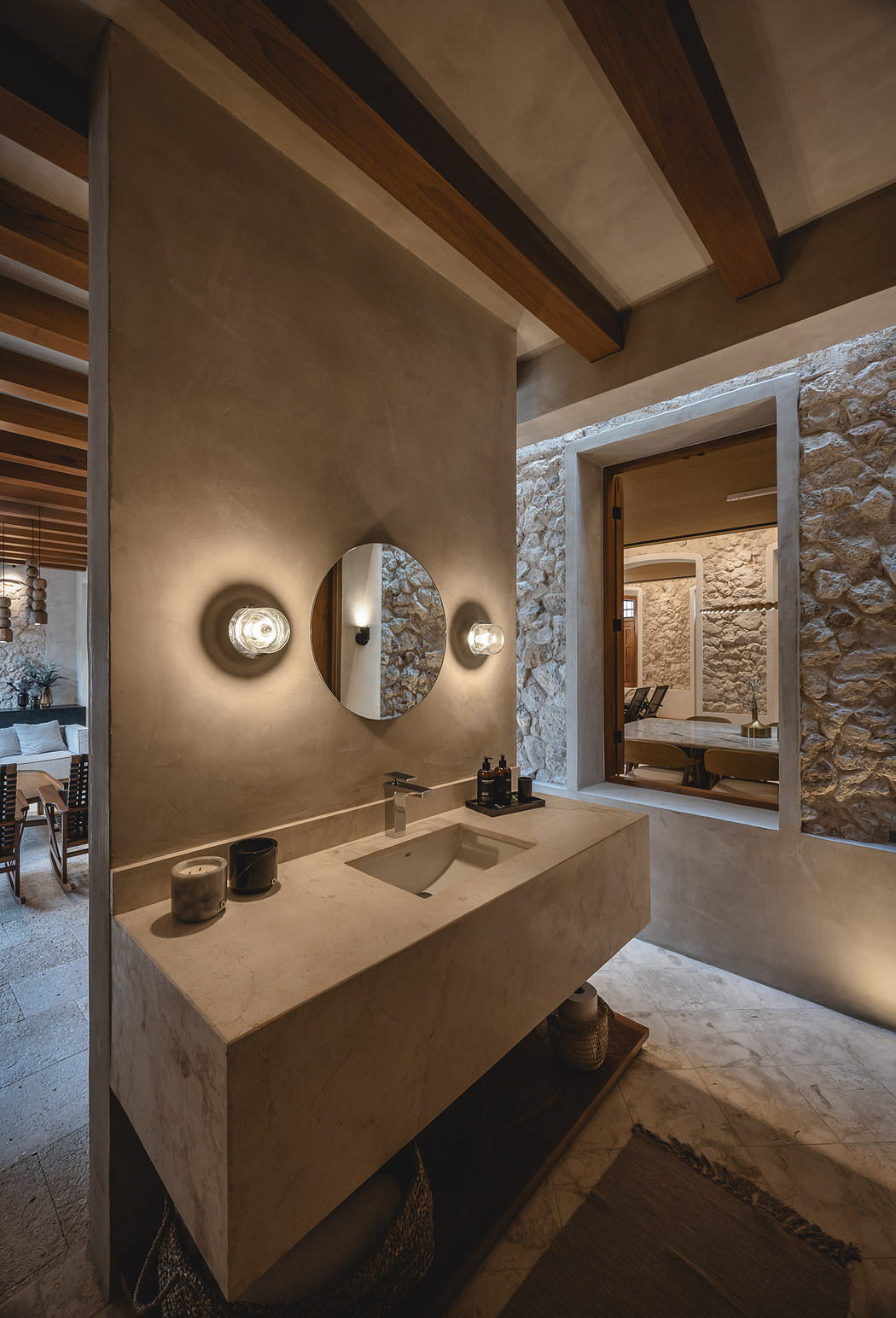Warm-toned rustic bathroom with stone walls, wooden beams, and a concrete vanity.