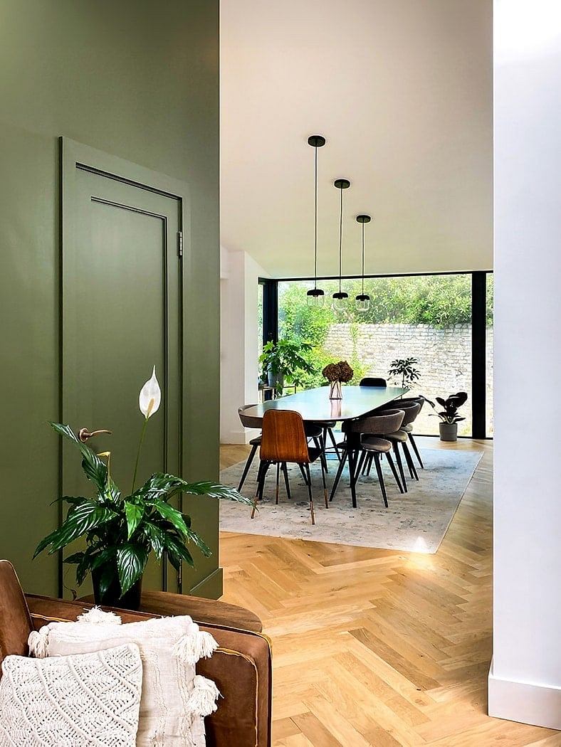 Contemporary dining space with herringbone wood floors, hanging lamps, and leafy plants.