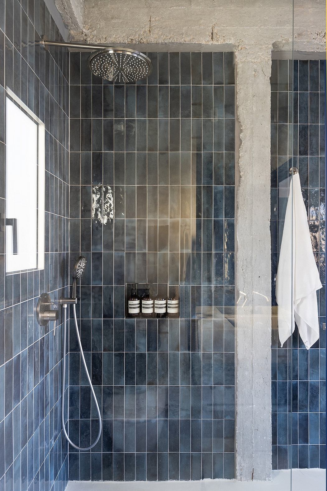 Monochromatic bathroom with floor-to-ceiling black tiles, circular shower head, and toiletry shelves.