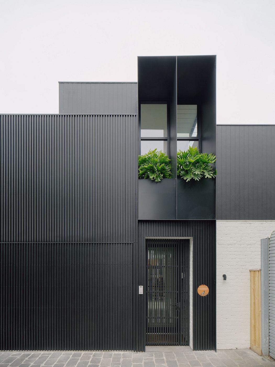 Modern minimalist building facade with vertical black panels, recessed planter boxes, and a wooden door.