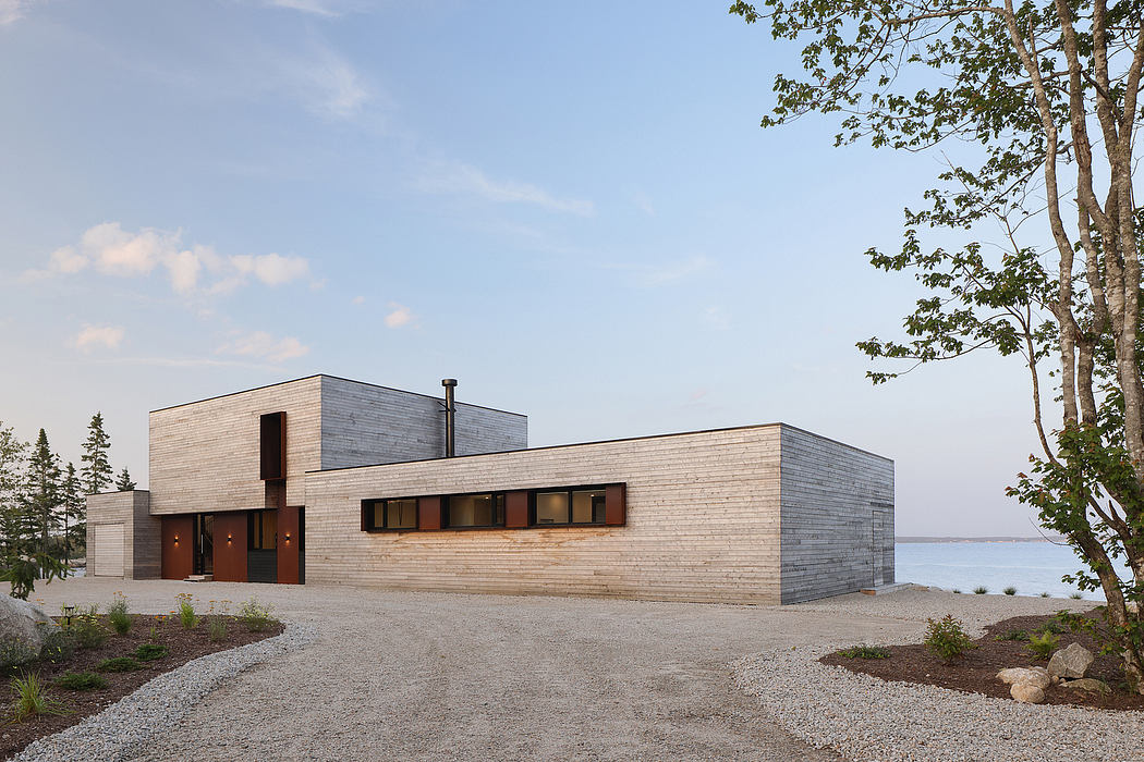 A modern, minimalist house with clean lines, large windows, and a gravel driveway.