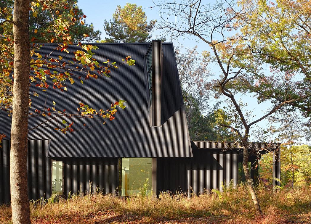 A modern, black-clad barn-like structure nestled in an autumn forest landscape.