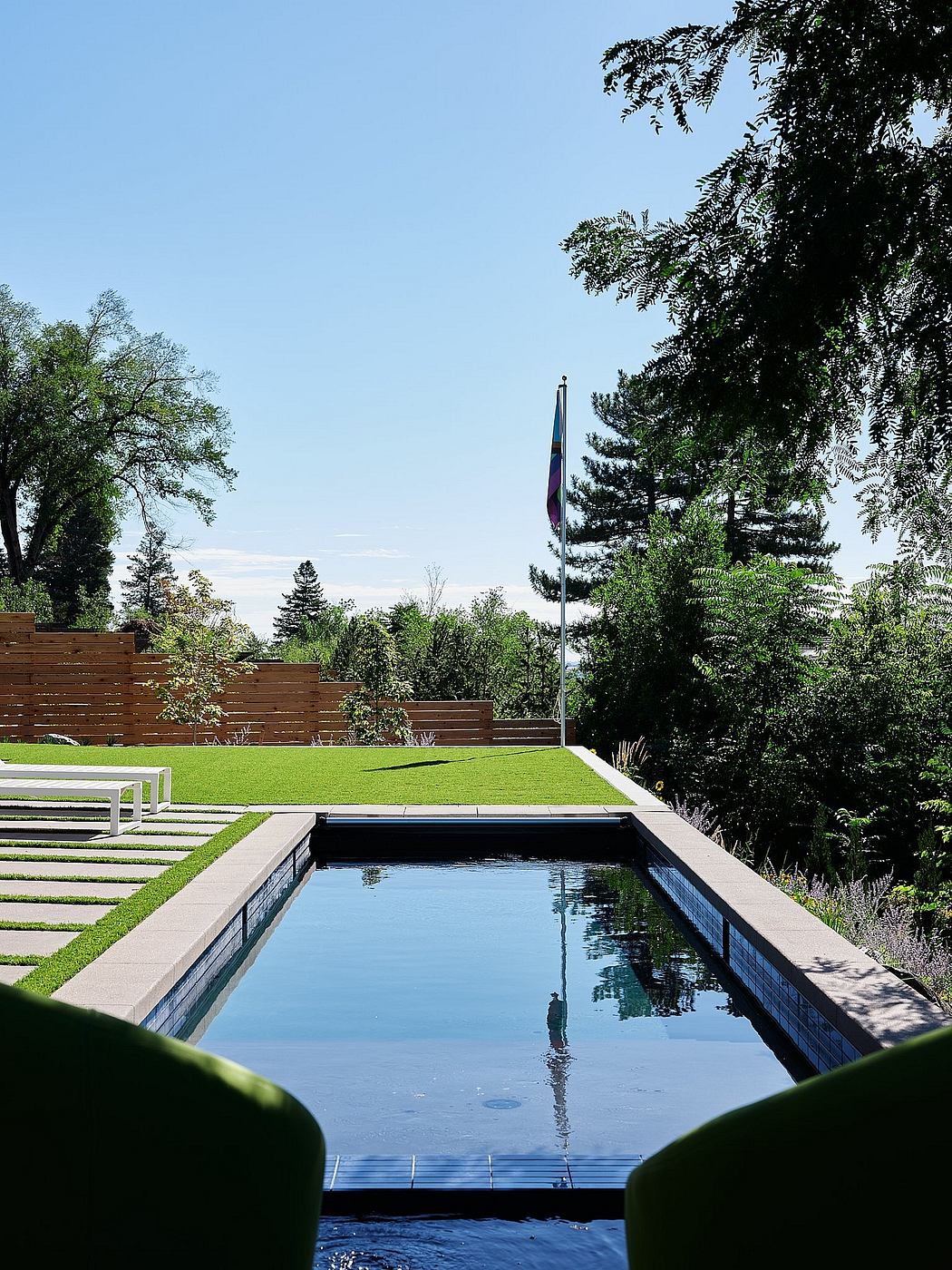 A tranquil outdoor setting with a rectangular pool, lush greenery, and a tall flagpole.
