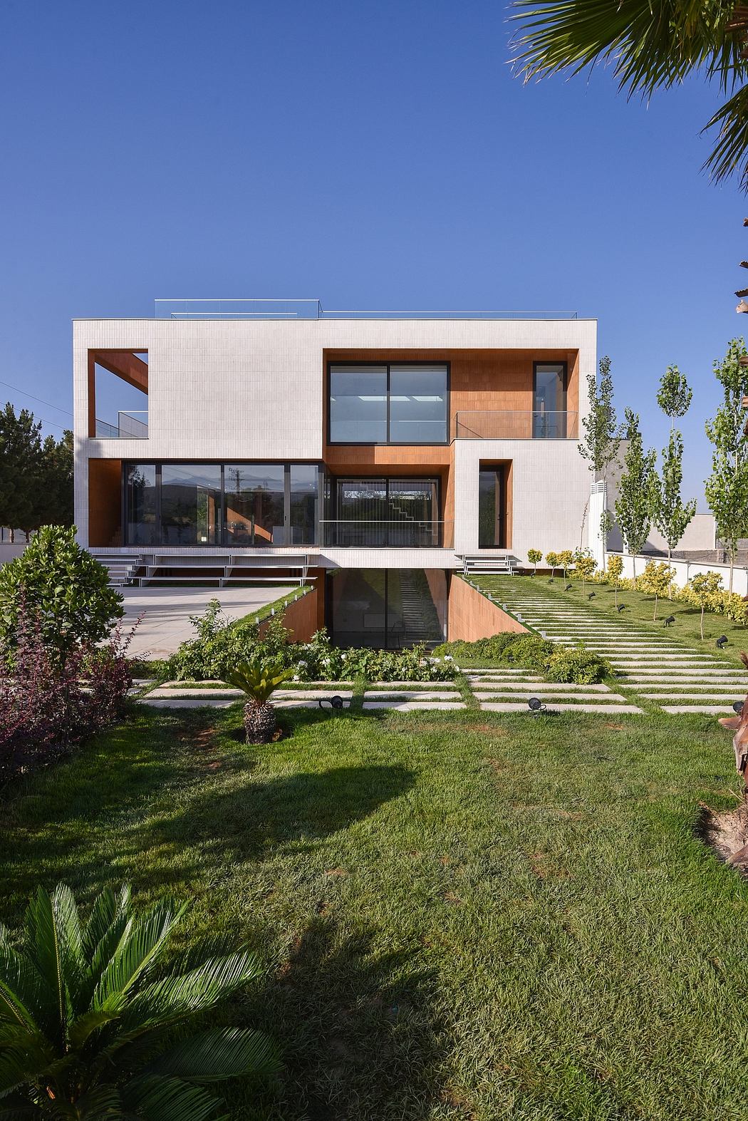 A modern, multi-level home with extensive glass, wood accents, and a lush landscaped exterior.