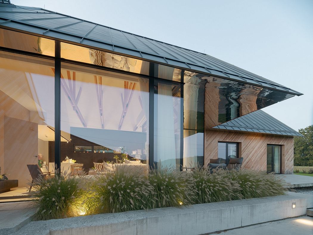 A modern glass-walled building with a sloping roof, surrounded by lush vegetation and landscaping.