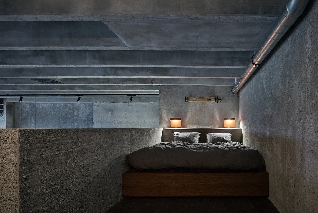 Cozy, minimal bedroom with exposed concrete walls and ceiling, recessed lighting, and wooden platform bed.
