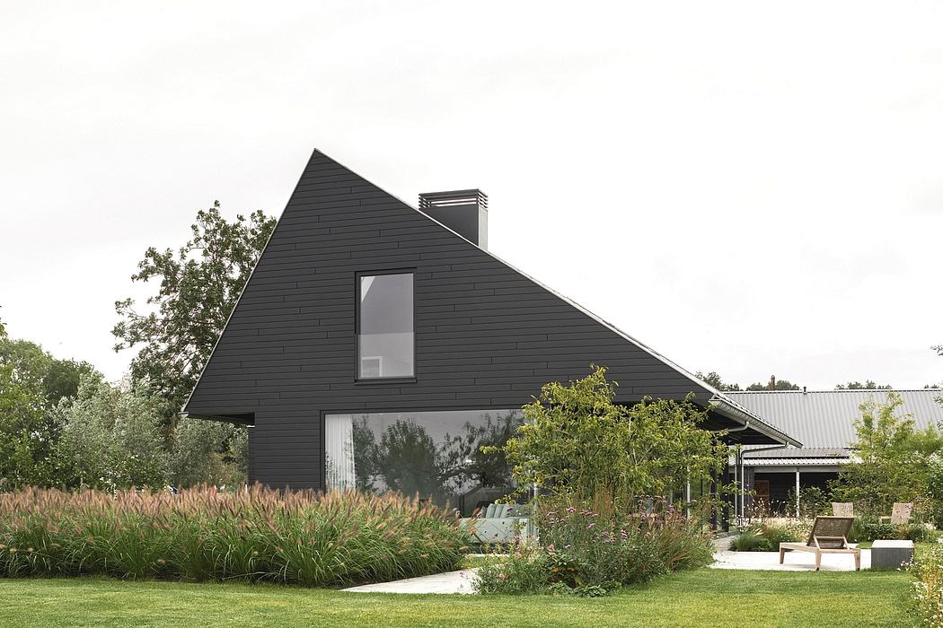 A modern, dark-clad structure with a prominent roofline, surrounded by lush greenery.