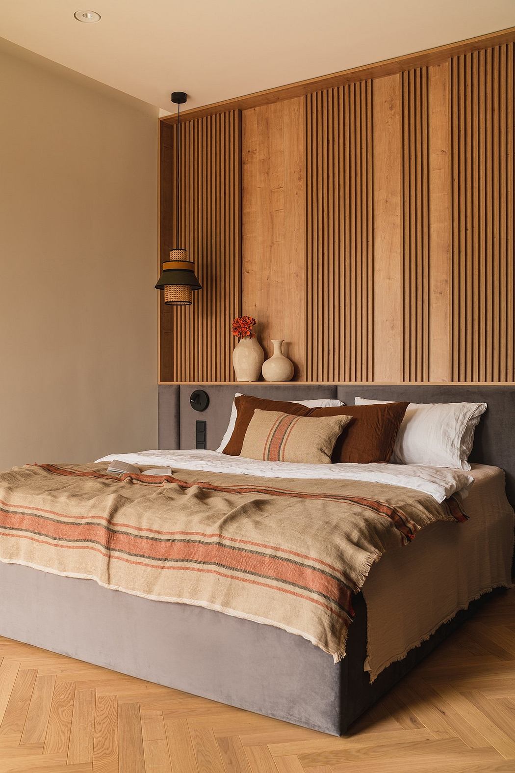 A cozy bedroom with warm wooden paneling, textured bedding, and a sleek pendant light.