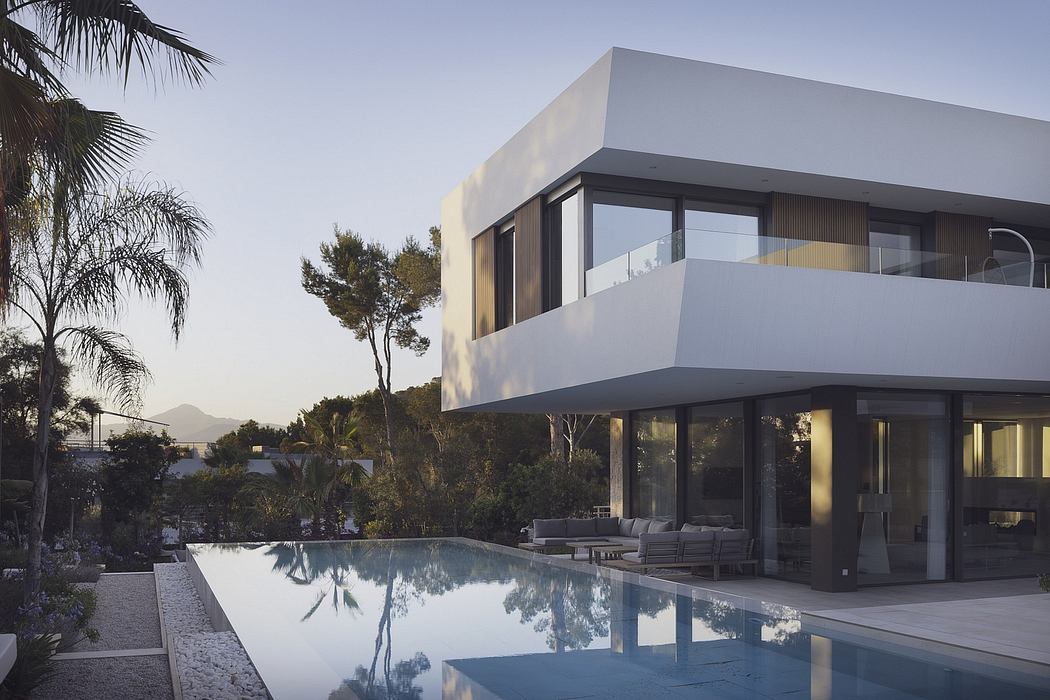 A modern, sleek villa with glass walls, a swimming pool, and lush surrounding vegetation.