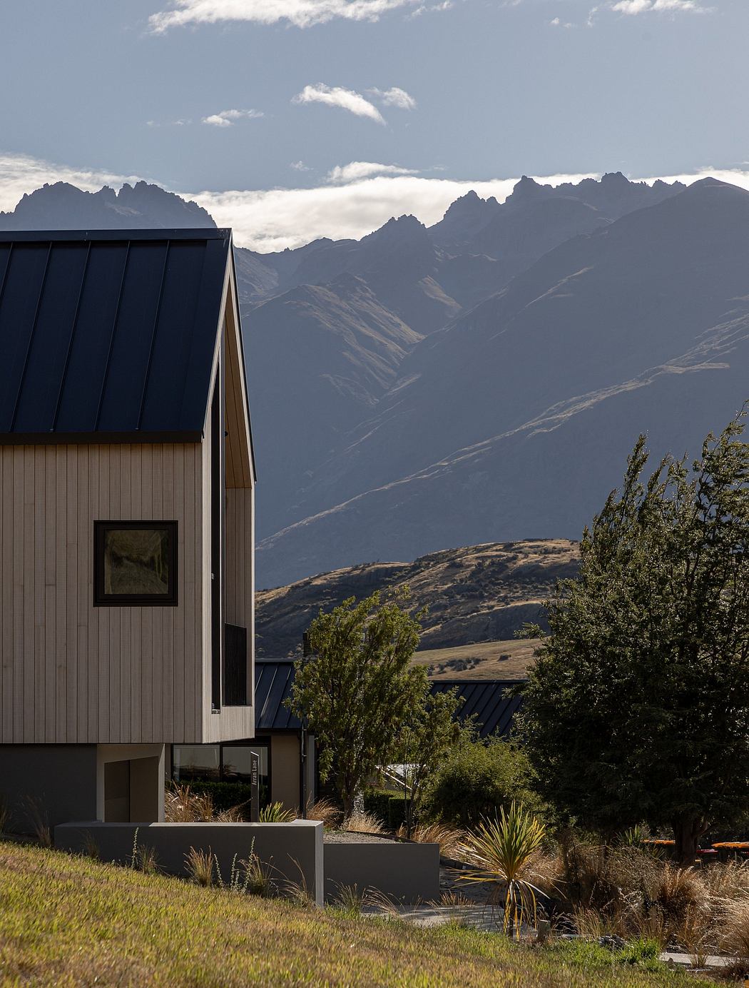 A modern, black-and-gray cabin with large windows overlooking rugged mountains.
