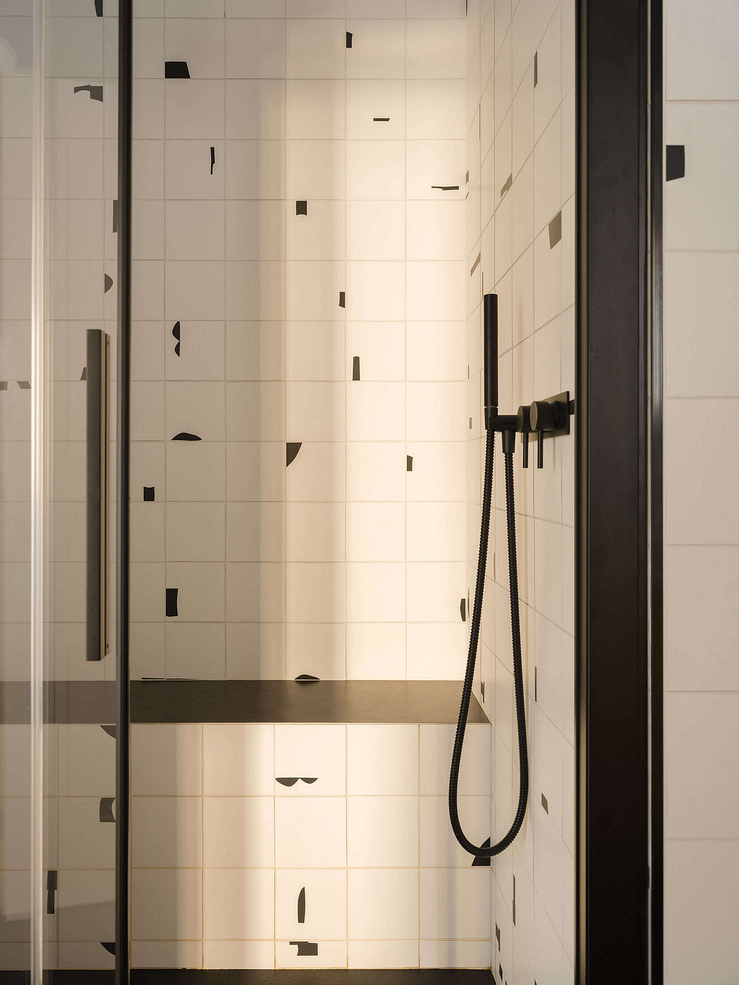 Modern, minimalist bathroom with white tile walls and a black shower fixture.