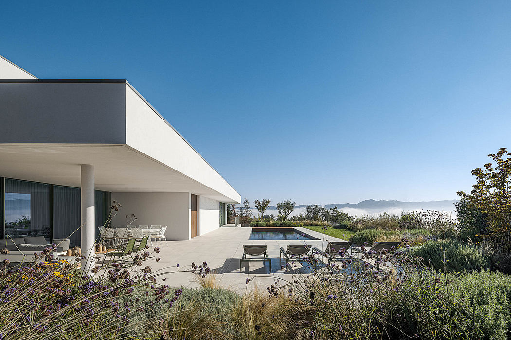 Modern, minimalist house with a pool, patio, and surrounding landscaping against a scenic backdrop.