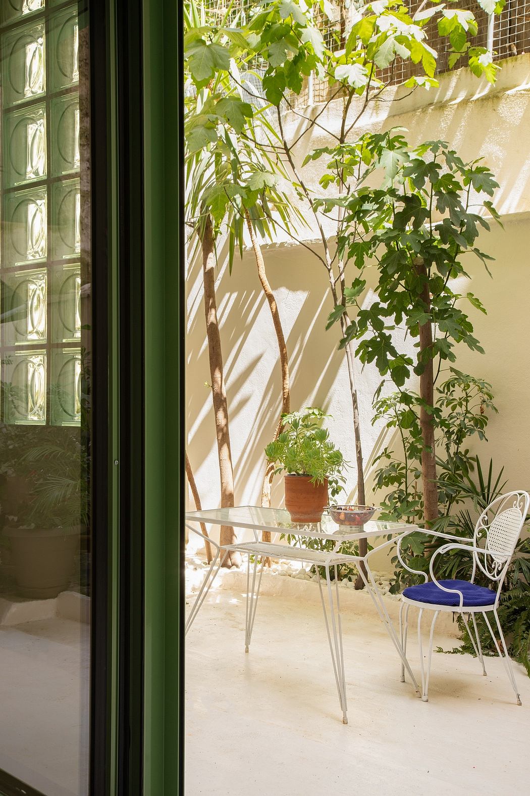 A cozy indoor patio with glass windows, lush greenery, and wrought-iron furniture.