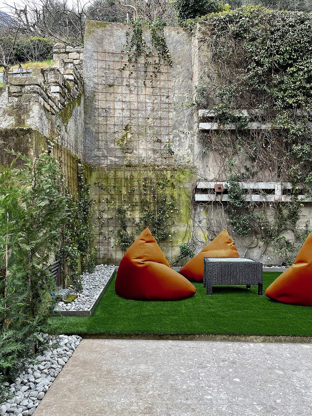 An outdoor seating area with orange beanbags, a black wicker chair, and a stone and wire wall feature.