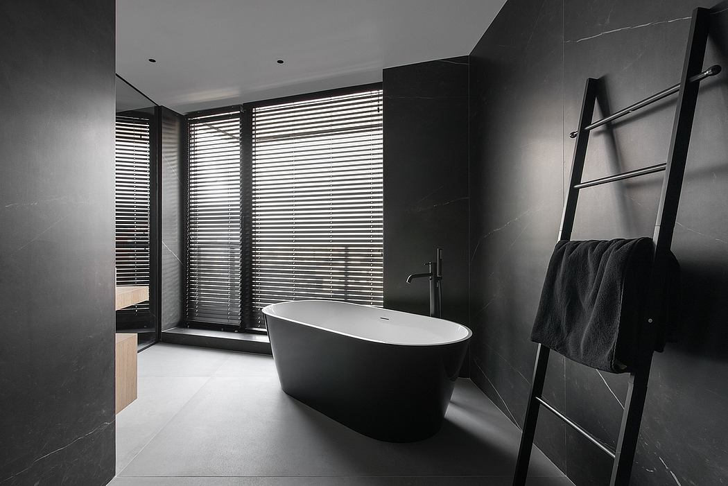 Sleek, modern bathroom with black marble walls, freestanding tub, and window blinds.