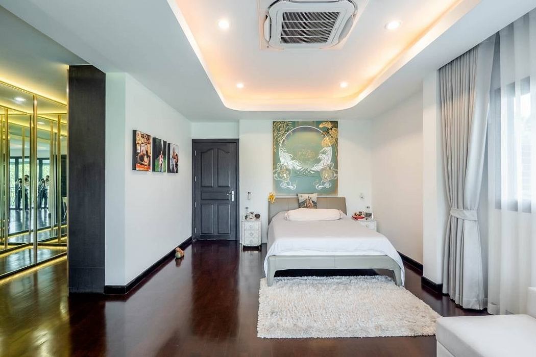 A modern, spacious bedroom with sleek furnishings, ornate artwork, and recessed lighting.