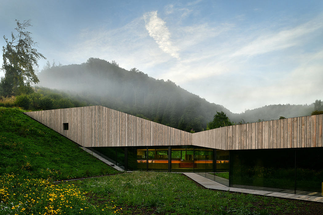 A modern, sleek wooden structure with a curved roof nestled in a lush, misty landscape.