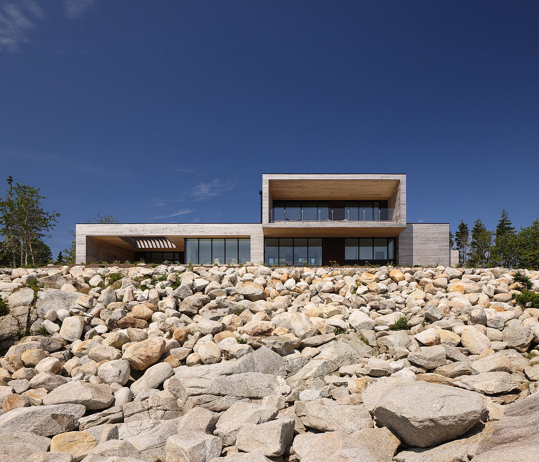 Modern architectural design featuring wooden elements, floor-to-ceiling windows, and a raised terrace with a rock-covered landscape.