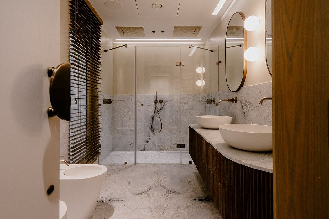 Modern, marble-lined bathroom with sleek vanity, circular mirrors, and glass enclosure.