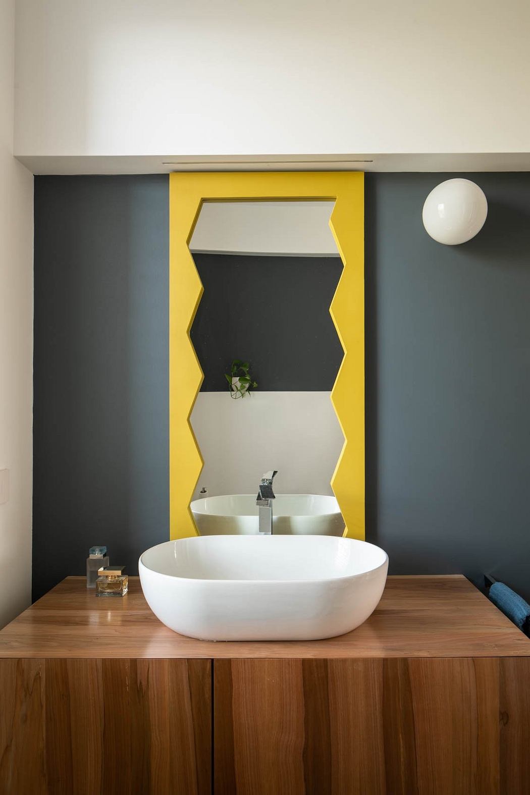 Minimalist bathroom design with a white oval sink, wooden countertop, and vibrant yellow frame.