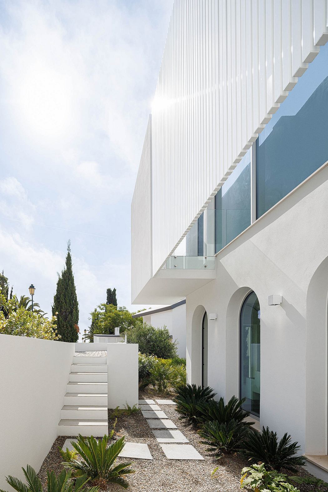 Modern white facade with sleek lines, arched windows, and a landscaped path leading to the entrance.