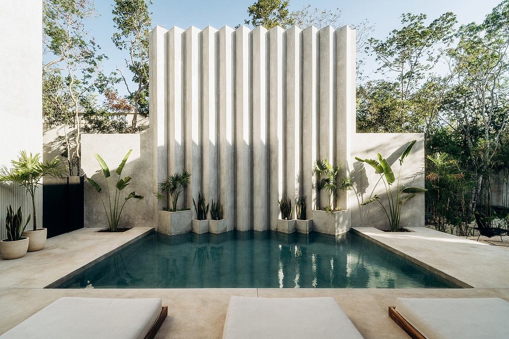 A modern, geometric swimming pool surrounded by lush greenery and a concrete water feature.