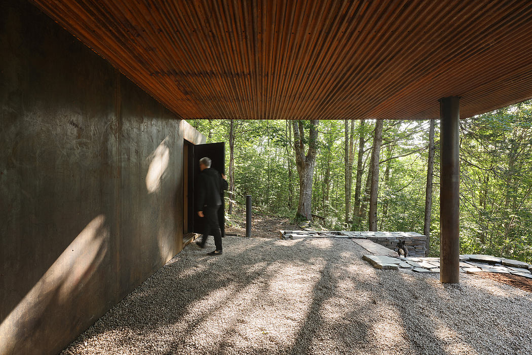 A rustic covered patio with a wooden ceiling, stone flooring, and a person entering through a doorway.