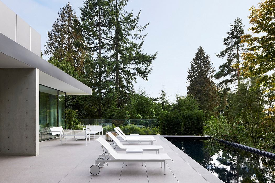 A modern, minimalist home with a pool, surrounded by lush greenery and tall trees.