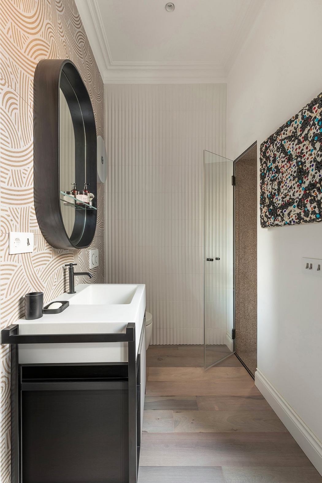 A modern bathroom with a round mirror, white vanity, and patterned wallpaper.