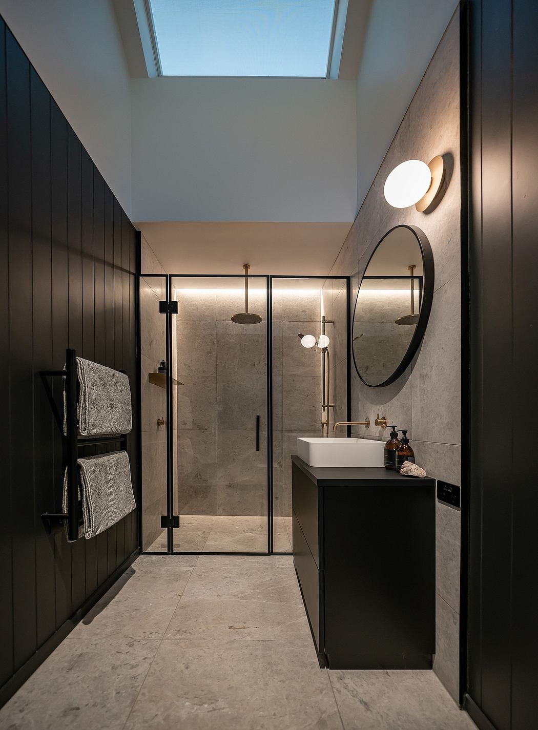 Sleek, modern bathroom with glass shower, marble vanity, and circular mirror.