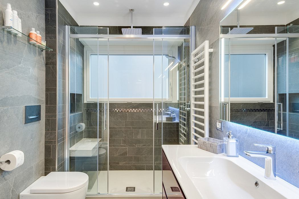Sleek, modern bathroom with gray tile, glass shower enclosure, and recessed lighting.