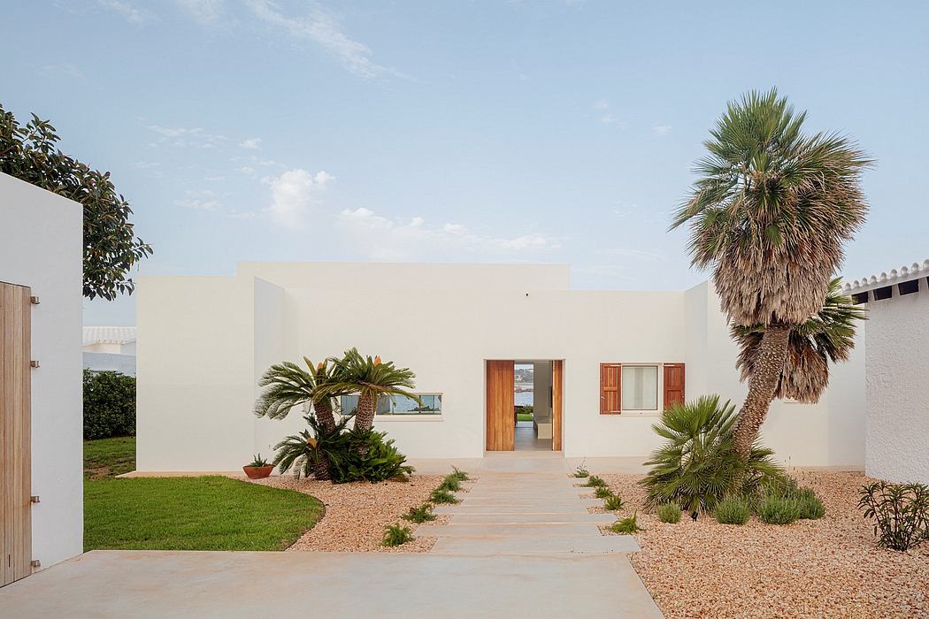 A modern, minimalist architectural design with palm trees and lush greenery surrounding the entrance.